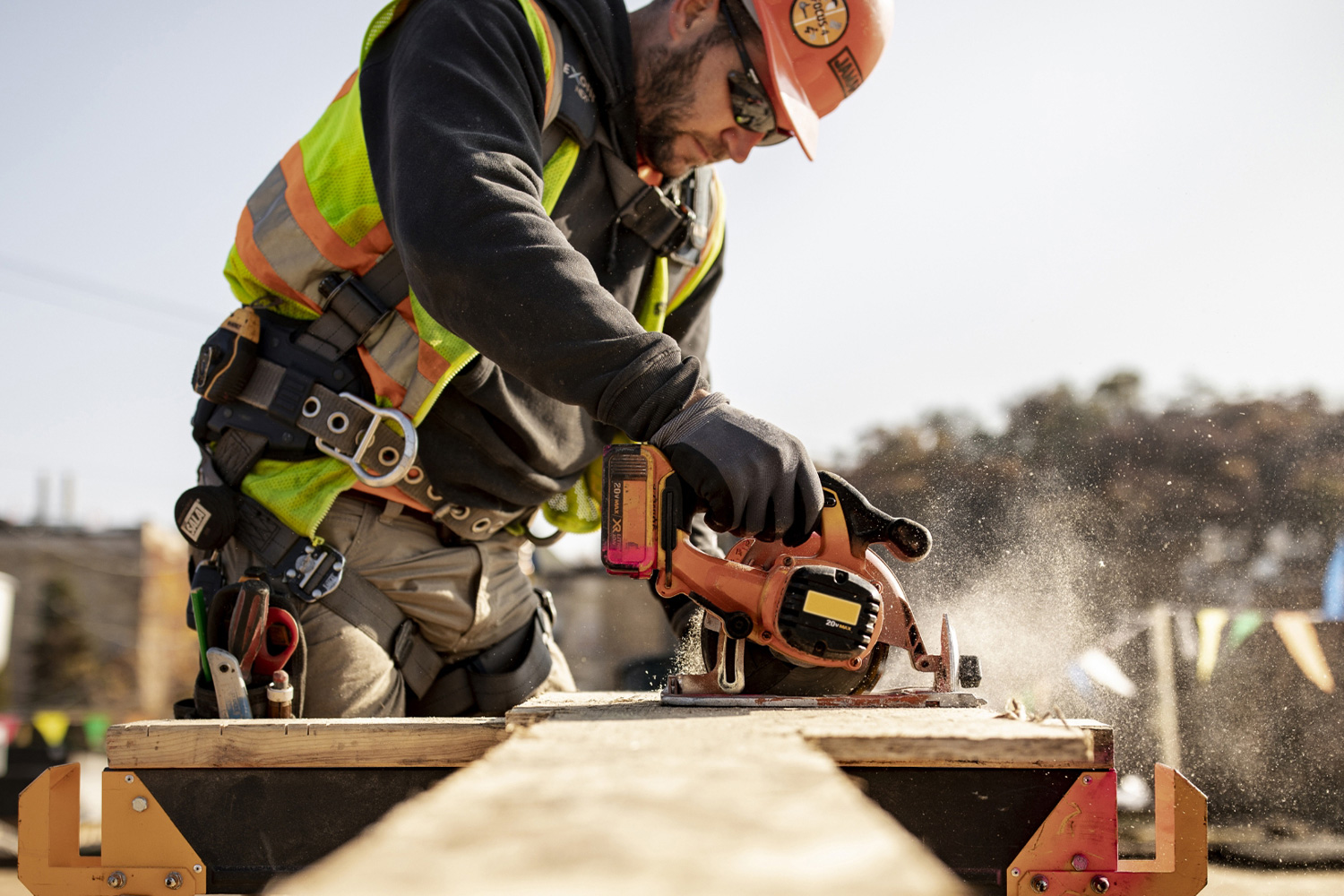 Sawdust flies as a coworker on a job site saws wood.