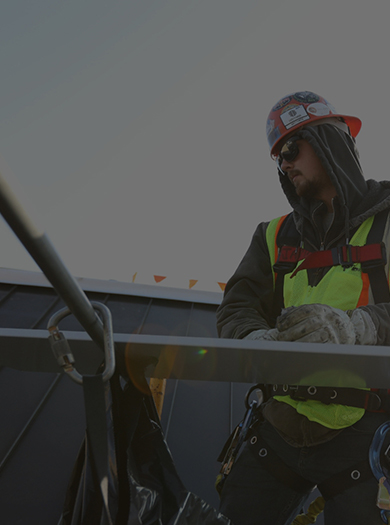 Two employees wearing safety gear and harnesses work on a roof.