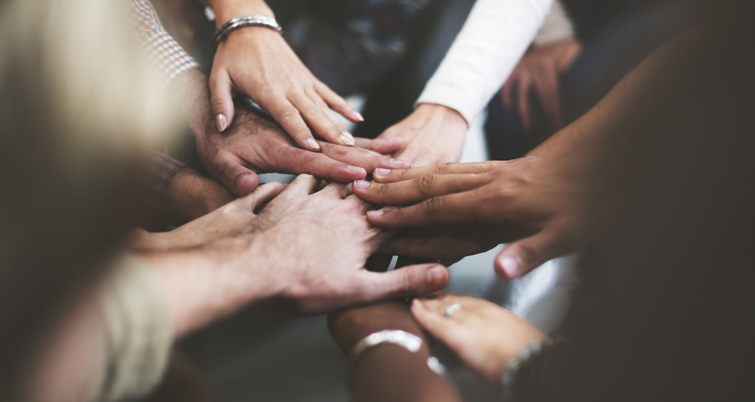 Coworkers are doing a hand huddle to symbolize teamwork.