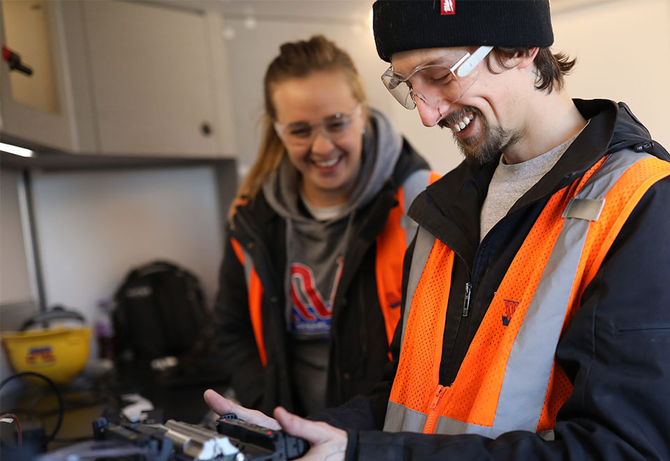 Two coworkers work together on a controller on their job site.